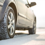 Nahaufnahme der Reifen und des Unterbodens eines PKW auf verschneiter Straße.