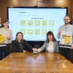 Mehrere Personen stehen vor einem Whiteboard mit einer Präsentation der Integriert-App versammelt, zwei davon drücken symbolisch den Startknopf des neuen Angebots.