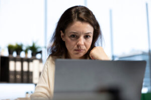 Frau in einem hellen Büro starrt mit genervtem Gesichtsausdruck auf einen Computerbildschirm