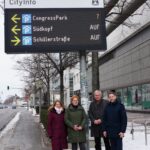 Vier Personen stehen unter einer LED-Tafel, die Parkmöglichkeiten in Wolfsburg anzeigt.