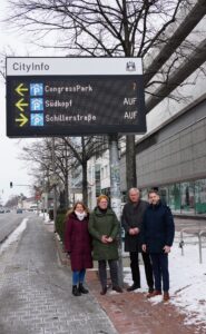 Vier Personen stehen unter einer LED-Tafel, die Parkmöglichkeiten in Wolfsburg anzeigt.