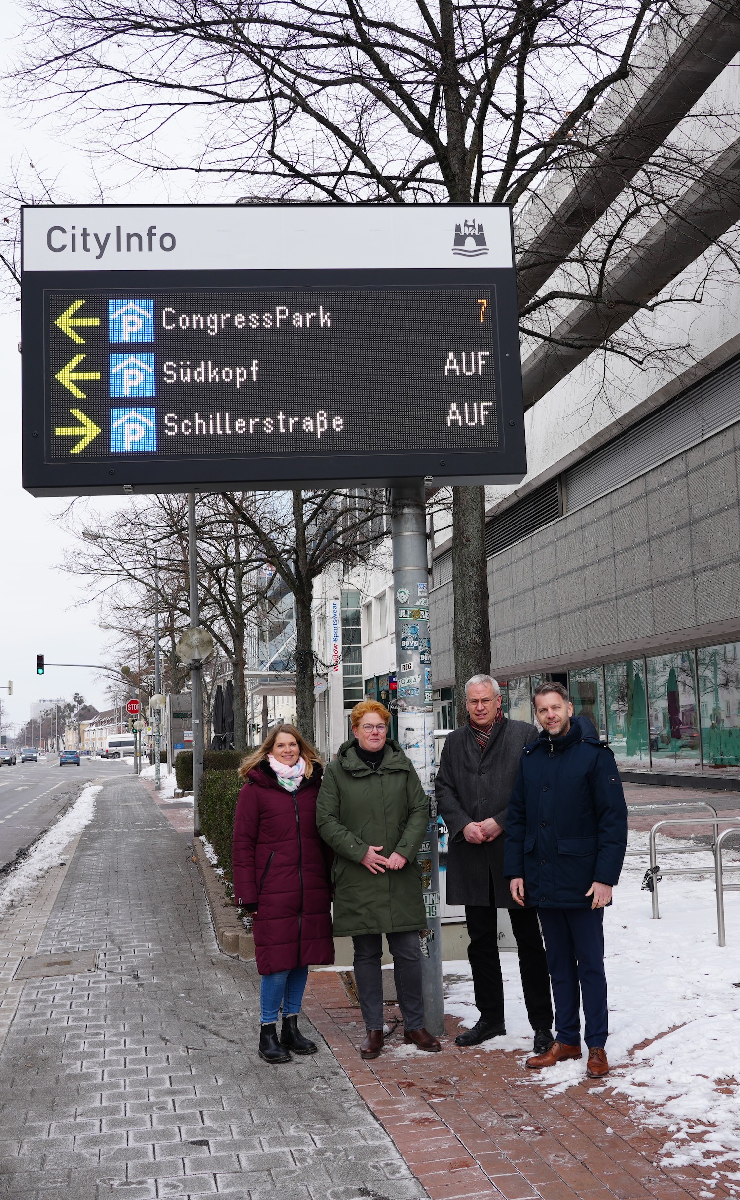 Vier Personen stehen unter einer LED-Tafel, die Parkmöglichkeiten in Wolfsburg anzeigt.