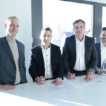 Vier Personen stehen nebeneinander an einem Tisch versammelt, zwei von ihnen unterzeichnen den Vertrag zwischen OWL-IT und regio iT.