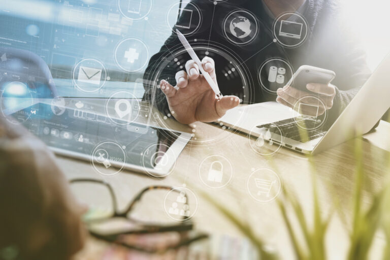 Montage: Schreibtisch, Laptops, Hände von Jacketttragenden Männern, Überlagerung mit diversen IT-Icons