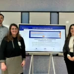 Auf dem Foto sind ein Mann und zwei Frauen vor einem digitalen Board zu sehen, das die Open-Data-Plattform der Landeshauptstadt Wiesbaden zeigt.