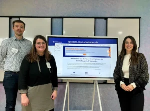 Auf dem Foto sind ein Mann und zwei Frauen vor einem digitalen Board zu sehen, das die Open-Data-Plattform der Landeshauptstadt Wiesbaden zeigt.