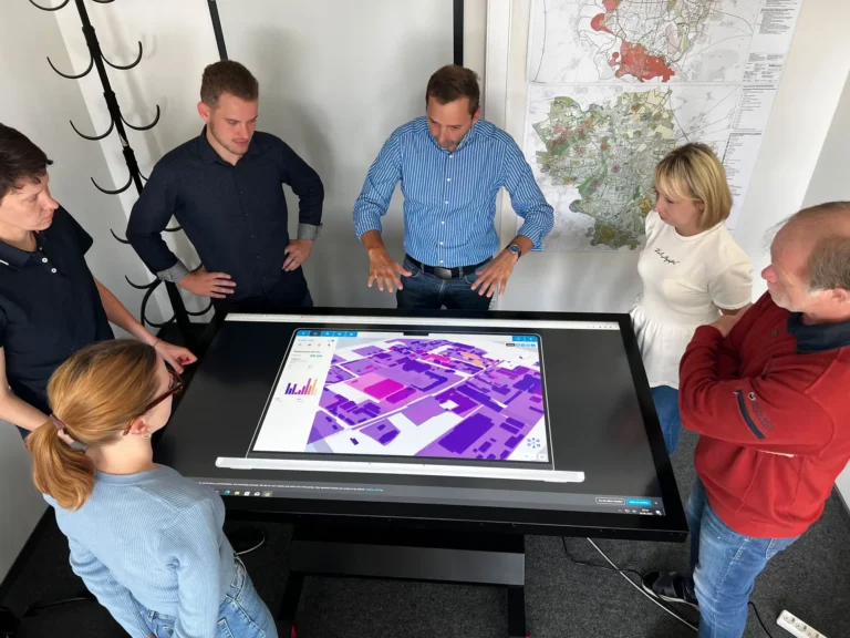 Mehrere Personen stehen um einen Datentisch versammelt, auf dem ein Stadtplan zu sehen ist.