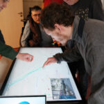 Mehrere Personen stehen um einen Maptable versammelt und bearbeiten eine Stadtkarte.