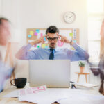 Meeting im Büro, Person am Kopfende des Tisches sieht sehr angespannt aus, die anderen sind unscharf (Bewegungsunschärfe)