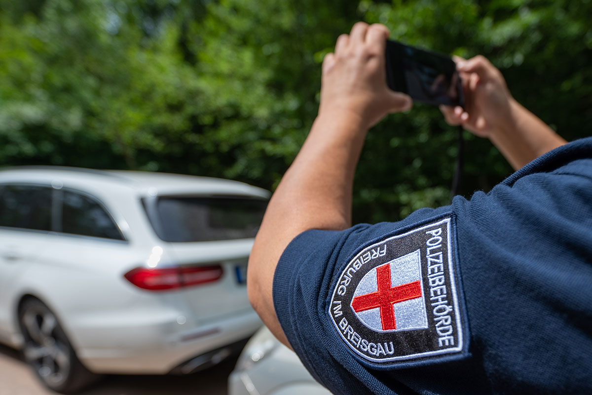 Eine bei der Polizeibehörde Freiburg um Breisgau angestellte Person nimmt mit der Smartphonekamera ein geparktes Fahrzeug auf.