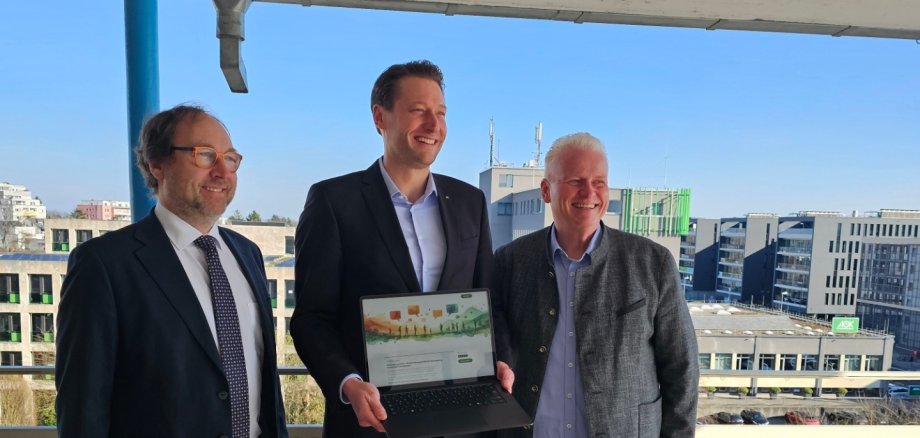 Die drei Stadtoberhäupter stehen zum Foto versammelt, OB Hetjes hält einen Laptop in den Händen auf dessen Bildschirm das Beteiligungsportal Seid Dabei eingeblendet ist.