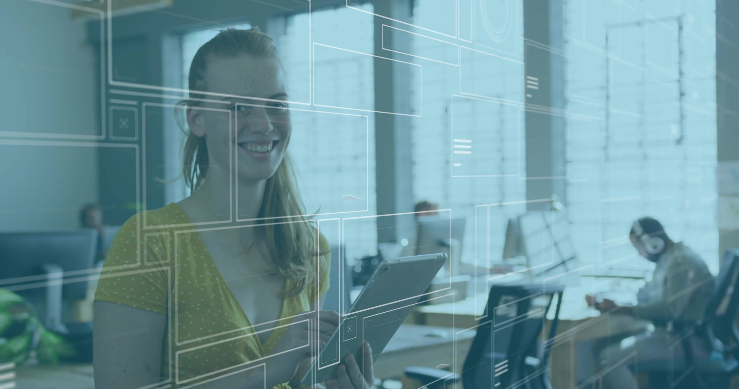 Eine lächelnde Frau hält ein Tablet in der Hand, im Hintergrund ist ein Großraumbüro zu sehen.