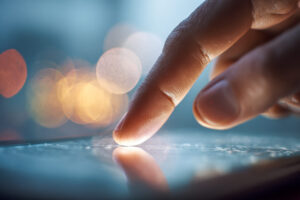 Finger tippt auf einem Smartphone, im Hintergrund Bokeh-Effekte