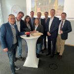 Mehrere Personen stehen um einen Tisch mit einem Startknopf versammelt.