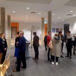 Mehrere Personen stehen in kleinen Gruppen versammelt in einem größeren Raum.