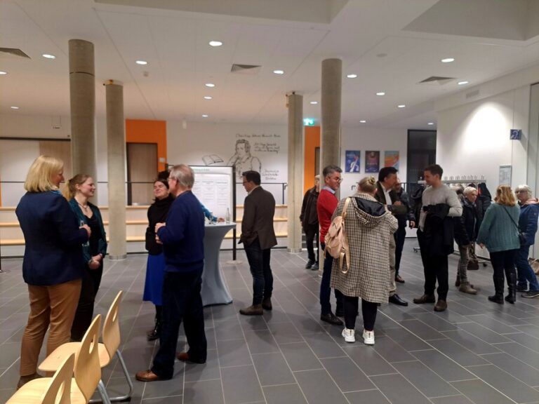 Mehrere Personen stehen in kleinen Gruppen versammelt in einem größeren Raum.