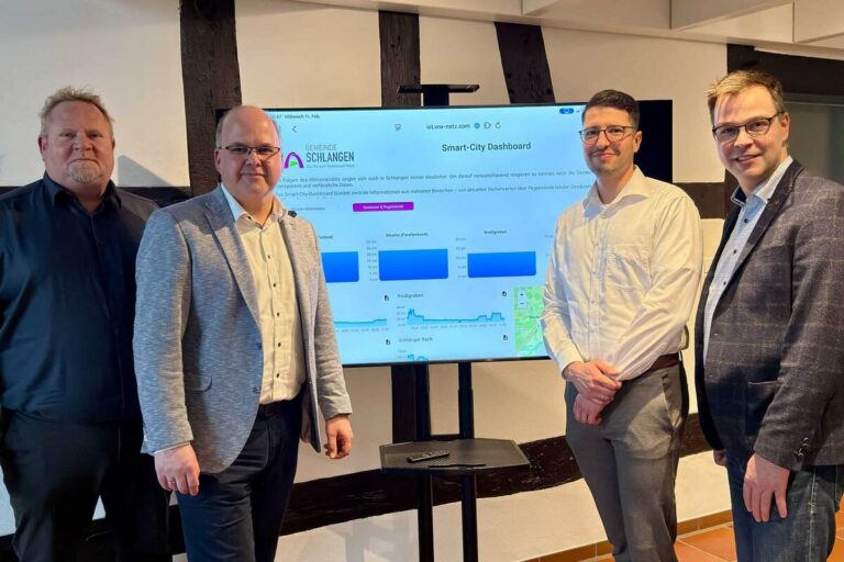 Vier Personen stehen um einen Monitor versammelt, auf dem das Smart City Dashboard für Schlangen zu sehen ist.