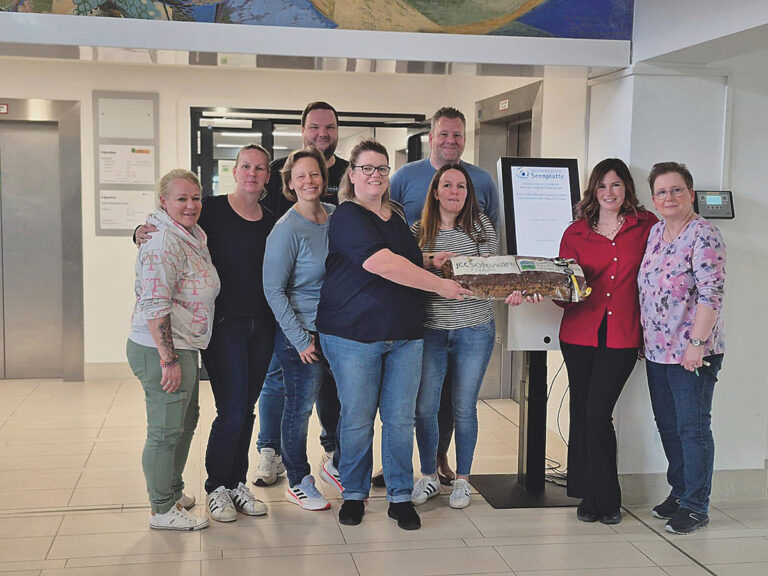Mehrere Personen stehen in einem Raum zum Gruppenfoto versammelt, im Hintergrund ist ein Anmeldeterminal zu sehen.