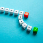 Spielwürfel mit aufgedruckten Pfeilen weisen den Weg hin zu einem Würfel mit grünem Häkchen.