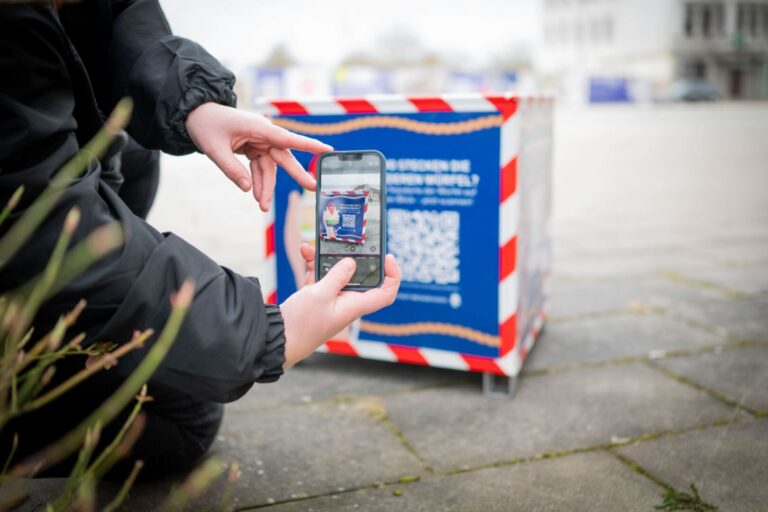 Eine Person scannt mit dem Smartphone den QR-Code eines Stadtwürfels in Bremerhaven.