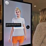 Der lebensgroße Avatar CAIA wird auf einem Monitor dargestellt. Der Avatar hat das Aussehen einer Frau.