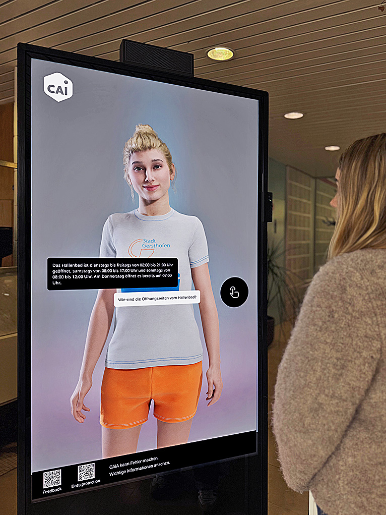 Der lebensgroße Avatar CAIA wird auf einem Monitor dargestellt. Der Avatar hat das Aussehen einer Frau.