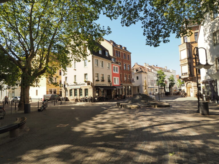 Großzügiger urbaner Platz ohne Menschen und Autos, aber mit Sonnenlicht und Baumschatten.
