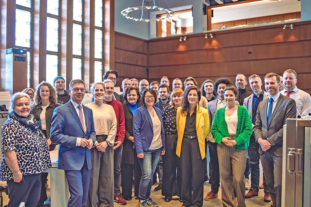 Mehrere Personen stehen in einem Raum zum Gruppenfoto versammelt.