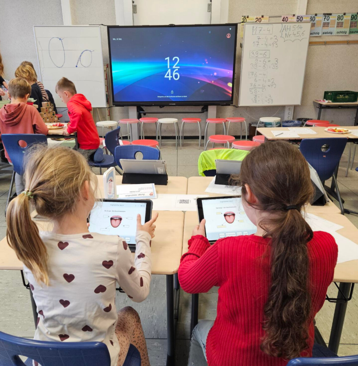 Mehrere Schülerinnen und Schüler arbeiten im Klassenzimmer mit Tablets.
