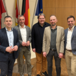 Fünf männliche Personen stehen in einem Besprechungsraum nebeneinander zum Foto versammelt.