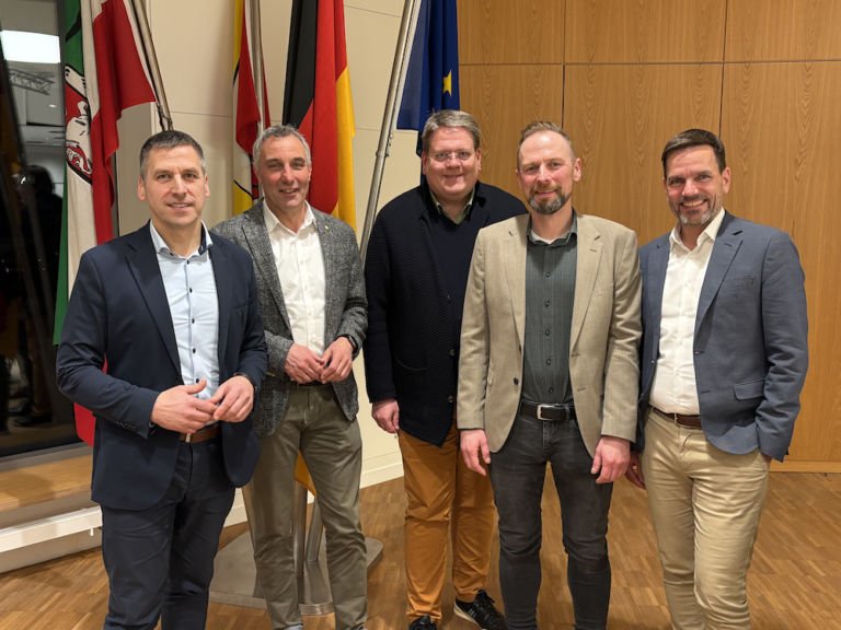 Fünf männliche Personen stehen in einem Besprechungsraum nebeneinander zum Foto versammelt.