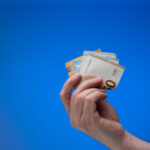 Hand, die Euronoten in die Höhe hält, blauer Hintergrund.