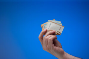 Hand, die Euronoten in die Höhe hält, blauer Hintergrund.