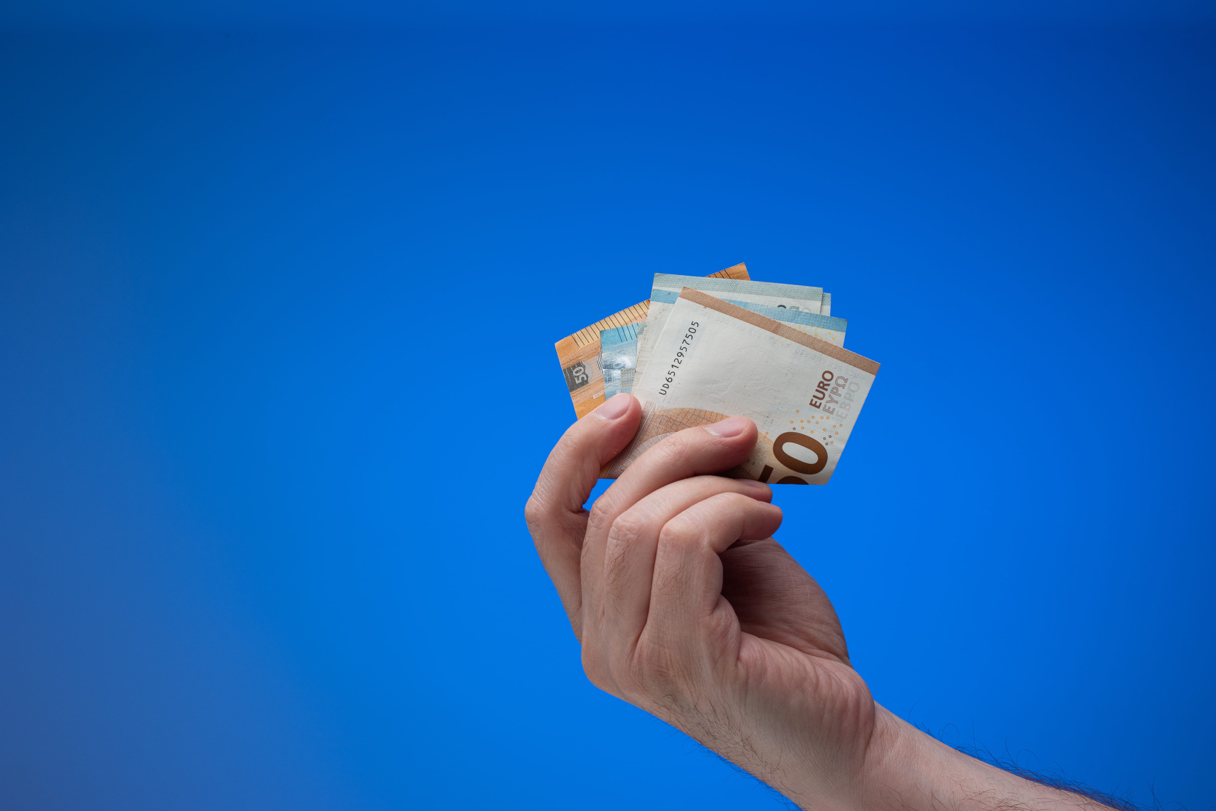 Hand, die Euronoten in die Höhe hält, blauer Hintergrund.