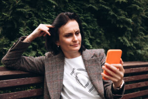 Ein Mädchen in einer braunen Jacke sitzt auf einer Bank und schaut oder liest etwas auf einem Smartphone.