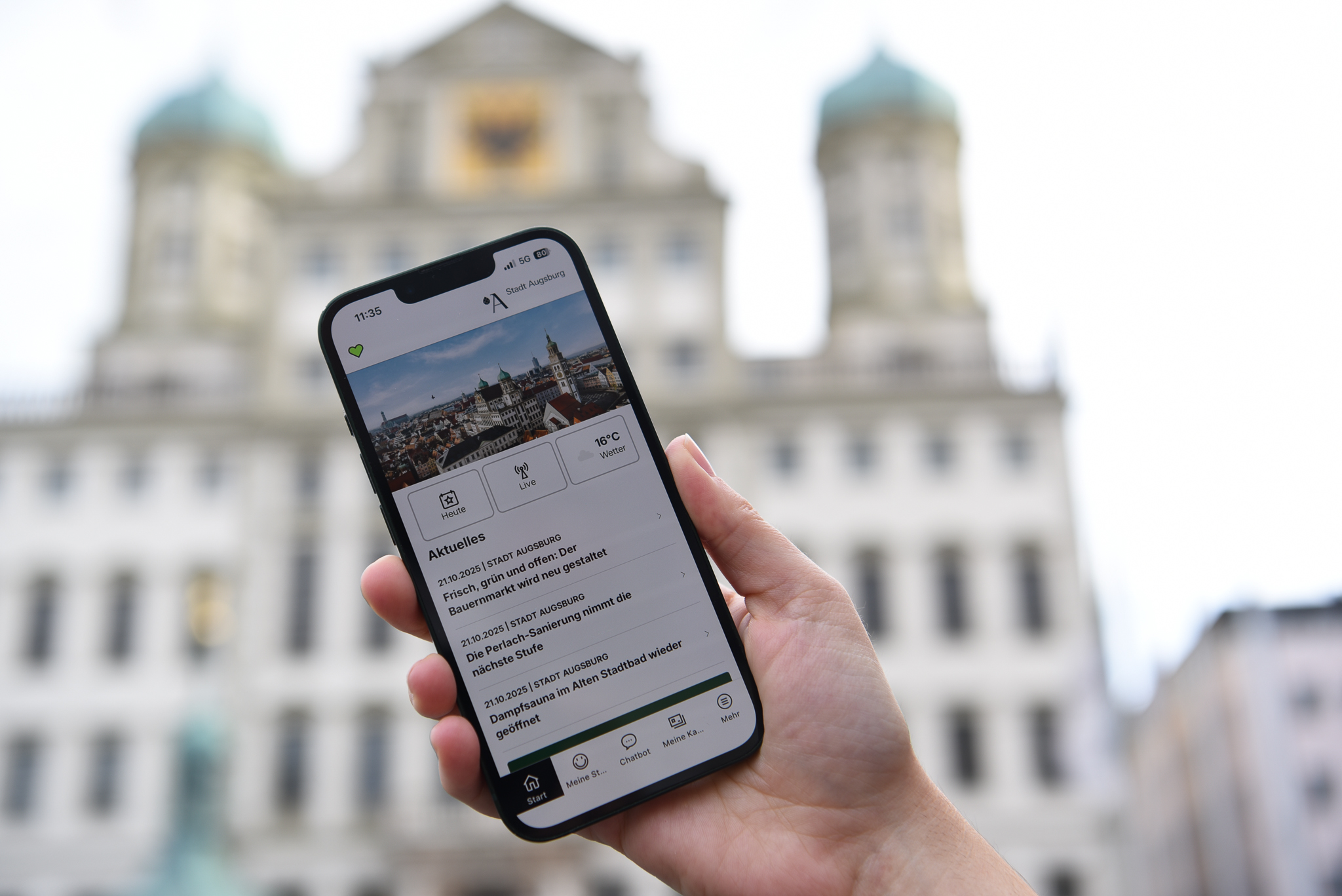 hand mit Smartphone mit Augsburg-App vor Augsburger Rathaus