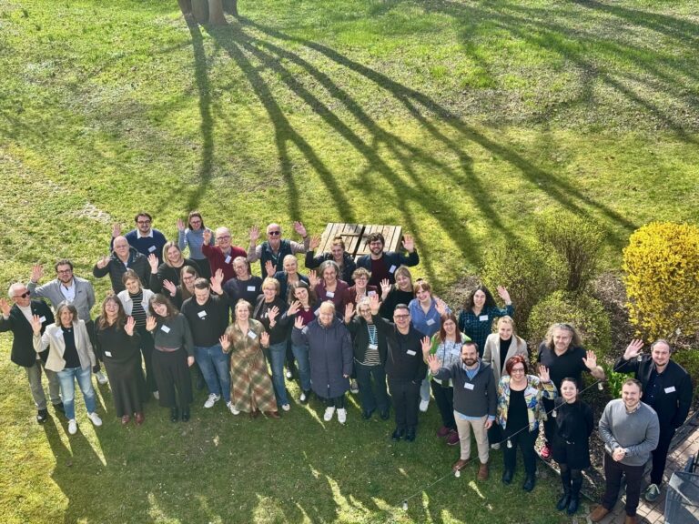 Gruppenfoto von wnkenden Menschen auf einer Wiese aus Vogelperspektive