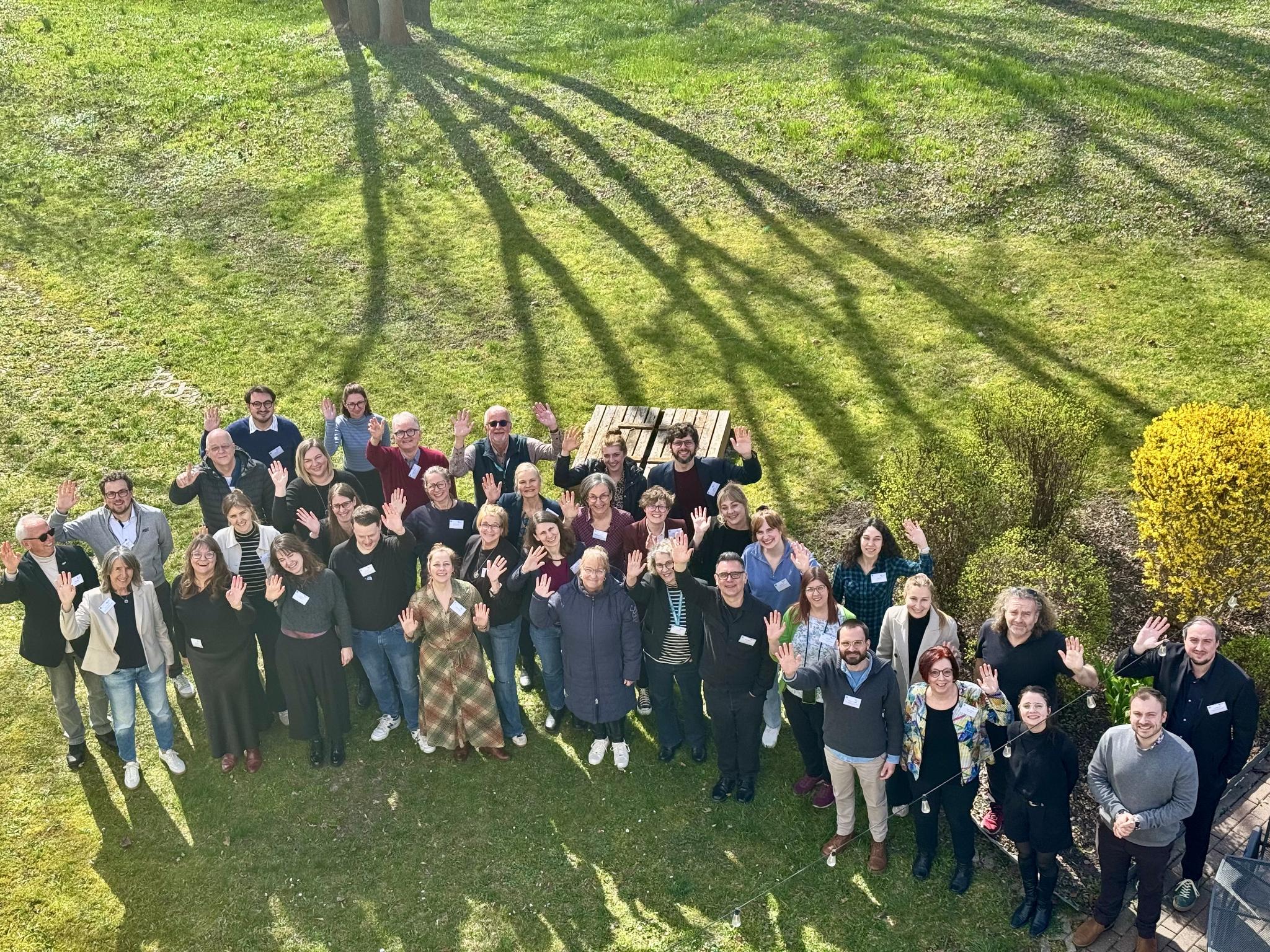 Gruppenfoto von wnkenden Menschen auf einer Wiese aus Vogelperspektive