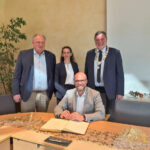 Mehring sitzend, drei Personen stehen hinter ihm, festlich-förmlicher Rahmen