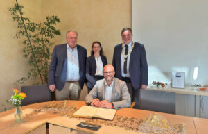 Mehring sitzend, drei Personen stehen hinter ihm, festlich-förmlicher Rahmen