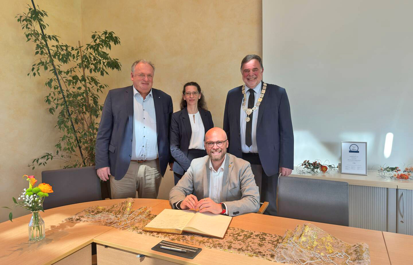 Mehring sitzend, drei Personen stehen hinter ihm, festlich-förmlicher Rahmen