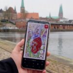 Hand mit einem Smartphone auf dem die interaktive Denkmalkarte zu sehen ist vor Lübecks Altstadt
