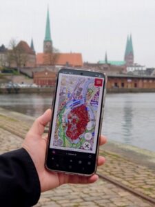 Hand mit einem Smartphone auf dem die interaktive Denkmalkarte zu sehen ist vor Lübecks Altstadt