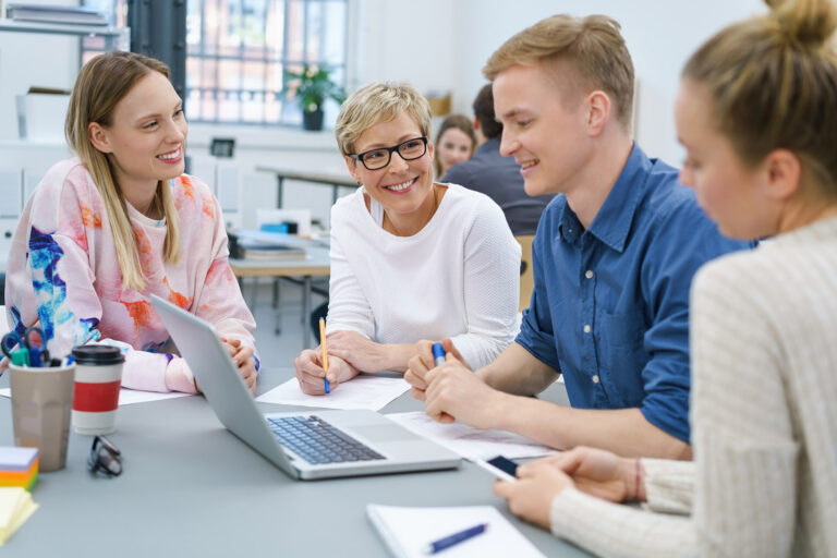 Team aus vier Personen sitzt an einem Tisch und tauischt sich aus.