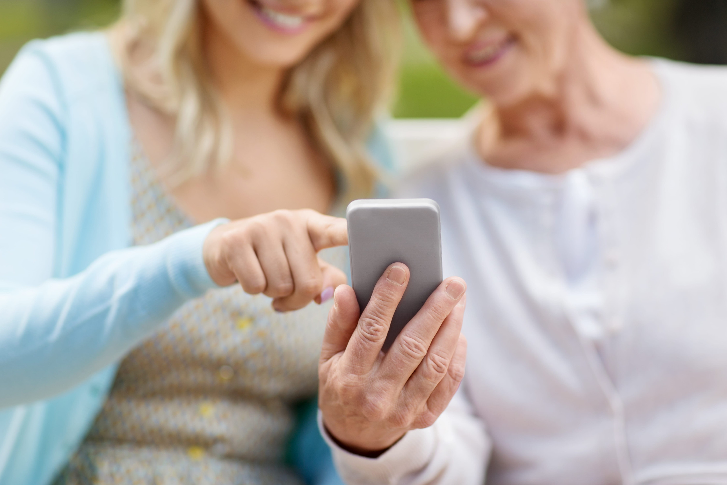 Tochter und Mutter im Seniorenalter im Park mit Smartphone