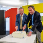 zwei Männer schneiden eine Torte an, im Hintergrund die 115_karlsruhe feiert die 115