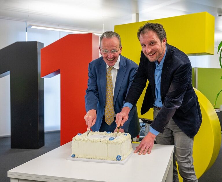 zwei Männer schneiden eine Torte an, im Hintergrund die 115_karlsruhe feiert die 115