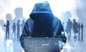 Illustration zum Thema Cybersicherheit: Im Vordergrund sitzt eine dunkel gekleidete Person mit tief ins Gesicht gezogener Kapuze vor einem Laptop. Im Hintergrund sind schemenhafte Silhouetten von Menschen zu sehen, die miteinander sprechen oder arbeiten. Überlagerte digitale Elemente und eine angedeutete Stadtlandschaft in Blau- und Grautönen vermitteln den Eindruck einer vernetzten digitalen Welt und symbolisieren die Bedrohung durch Cyberangriffe auf Organisationen und Verwaltungen.