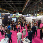 Blick in eine belebte Messehalle mit pinkfarbenem Bodenbelag