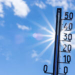Thermometer, das knapp 40 Grad anzeigt, im Gegenlicht gegen einen blauen Himmel und strahlende Sonne fotografiert